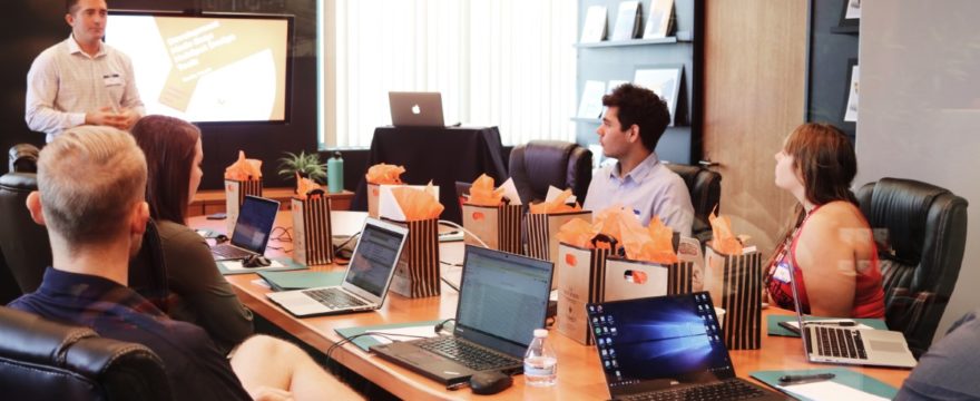 people around table with laptops facing presenter speaking